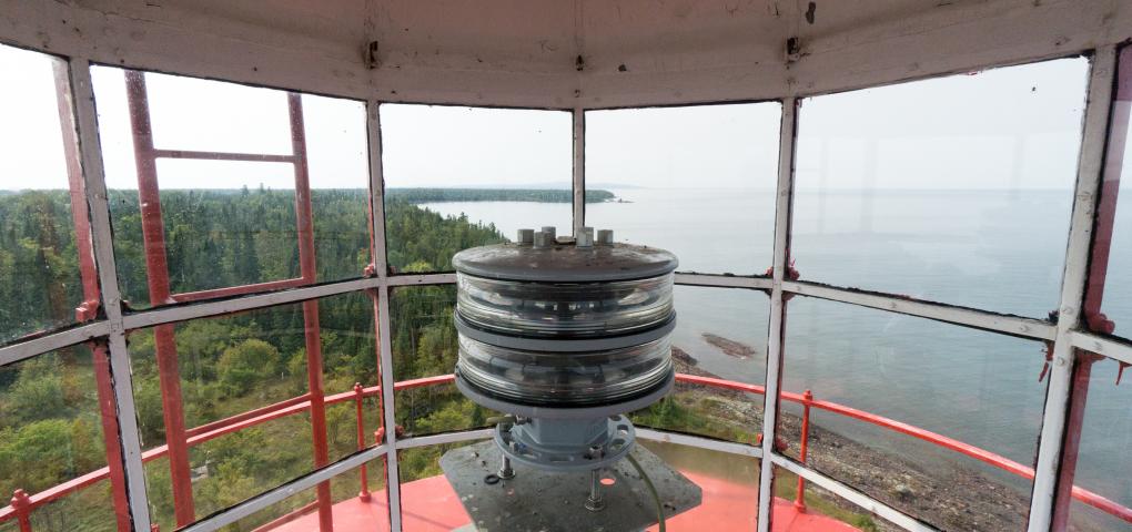 image looking out at the water from the tower with vantage point behind the lantern, red interior stark contrast to natural colors outdoors