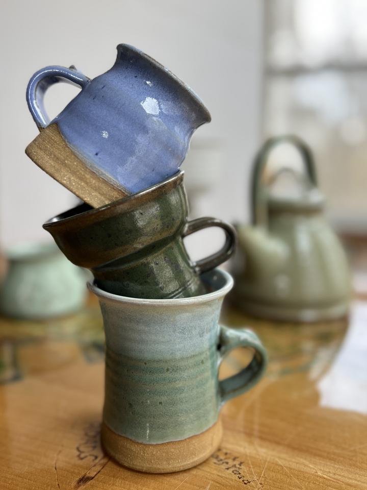 A stack of Gordon Borsvold mugs, with other handmade studio pottery in the background.